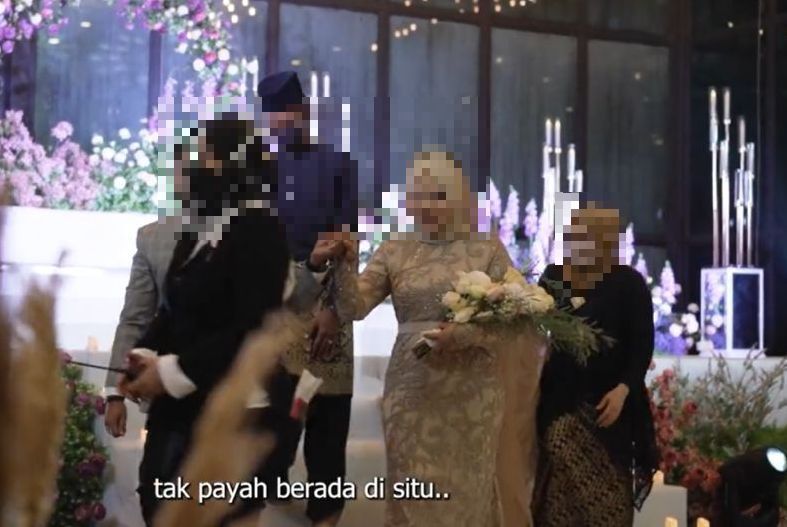 Koordinator majlis itu dilihat melintasi pasangan pengantin yang sedang bergerak ke meja makan