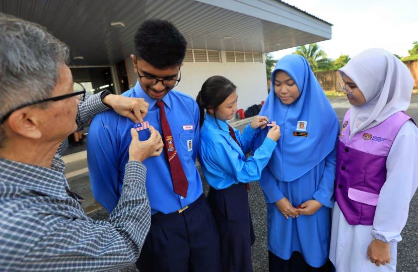 Guru Tan Say Lee (kiri) membantu menyematkan lencana Jalur Gemilang pada pakaian seragammurid, T. Kiisyan.