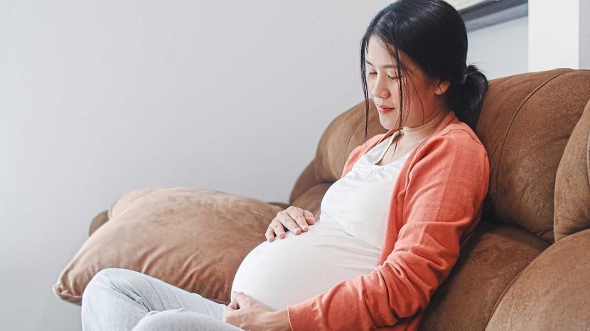 Young Asian Pregnant woman holding her belly talking with her child. Mom feeling happy smiling positive and peaceful while take care baby, pregnancy lying on sofa in living room at home concept.