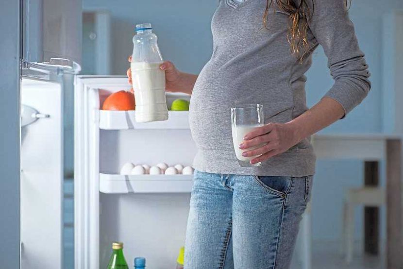 Pregnant woman near fridge looking for food and snacks at night