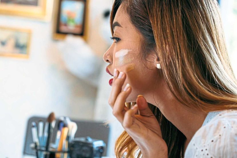 Closeup young Asian woman with red lips applying corrector on face on blurred background