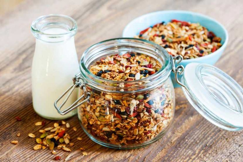 Homemade granola in open glass jar and milk or yogurton rustic wooden background
