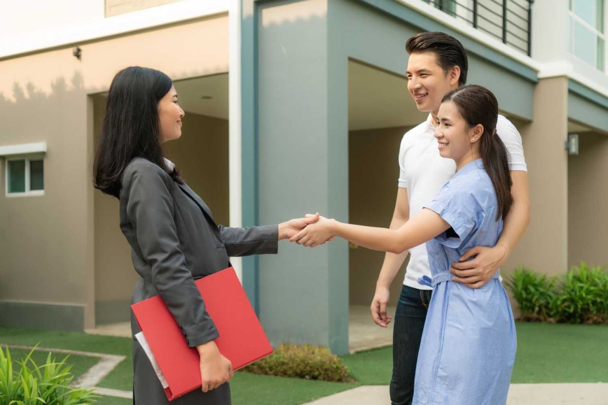Happy Asian couple looking for their new house and shake hands with real estate broker after a deal. Young couple handshaking real estate agent after signing contract for buy house.
