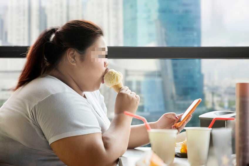 Side view of obese woman enjoying leisure time with a mobile phone and ice cream cone in the cafe