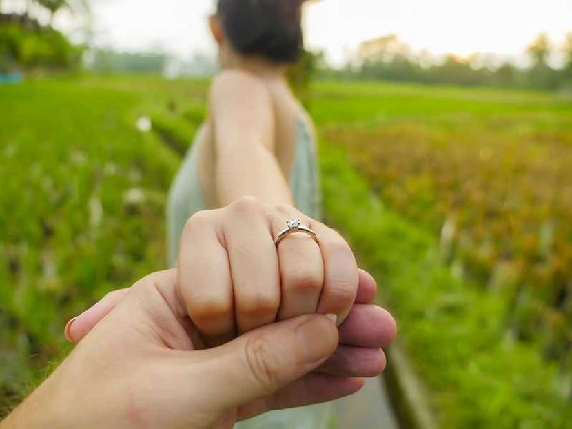 close up couple hands man holding happy fiance hand with diamond engagement ring on her finger after wedding proposal at tropical beautiful and romantic spot proposing marriage