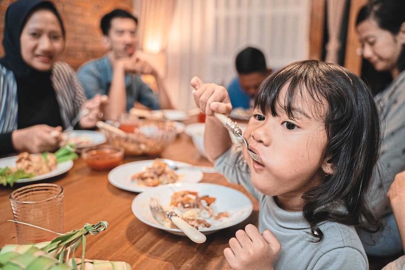 child daughter eating by herself during dinner. asian family at the background