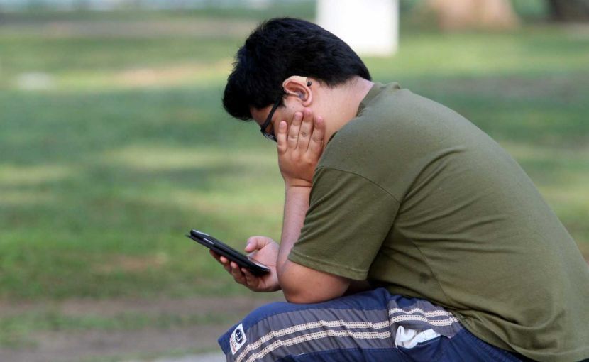A man playing games on his handphone at a park in Ipoh.