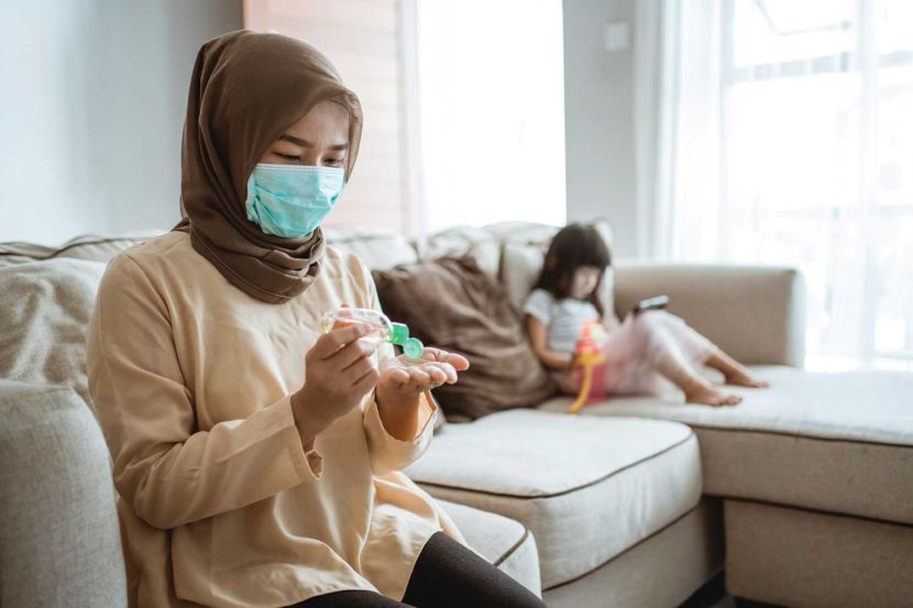 muslim woman with masks applying hand sanitizer at home